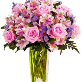 Pink roses and mixed purple flowers in a clear glass vase