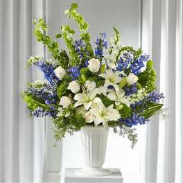 White lilies and roses arranged with blue flowers in a white vase