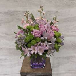 Pink roses and lavender flowers arranged in a purple vase