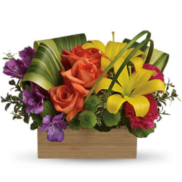 Low rectangular arrangement of yellow lilies, orange roses, purple blooms, and green mums in a wooden box