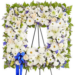 White floral standing wreath on an easel with a blue ribbon