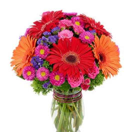 Bright bouquet of red gerbera daisies and mixed pink and purple flowers in a clear glass vase