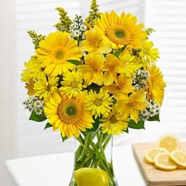 Bright yellow bouquet with gerbera daisies and alstroemeria in a clear vase with a lemon in the water