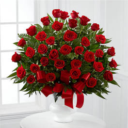 Red roses arranged in a white vase with a red ribbon