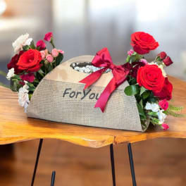 Flower arrangement in a burlap gift box with red roses and pink blooms