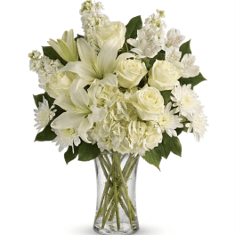 All-white bouquet of lilies, roses, hydrangeas, and other blooms arranged in a clear glass vase