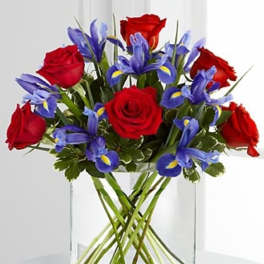 Red roses and blue irises in a clear glass vase