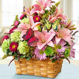 Basket of pink lilies, green carnations, and mixed blooms with colorful butterfly accents.