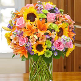 Bright mixed bouquet with sunflowers, orange lilies, and pink roses in a clear glass vase