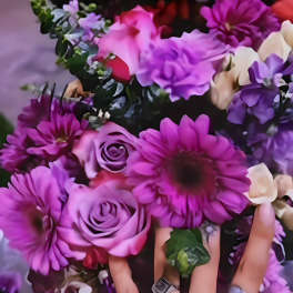 Hand holding a bouquet of purple flowers and roses