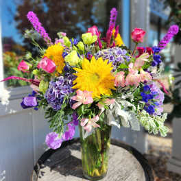 Colorful mixed bouquet in a clear glass vase with sunflowers and hydrangeas