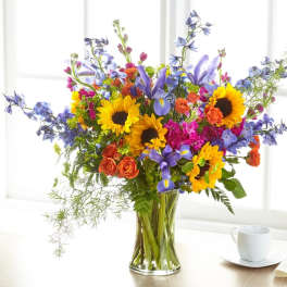 Colorful bouquet with sunflowers, roses, and purple flowers in a glass vase