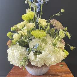 Tall floral arrangement with white hydrangeas, blue delphinium, and green blooms in a vase