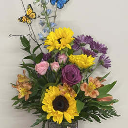 Mixed bouquet in a square glass vase with sunflowers, roses, and butterflies