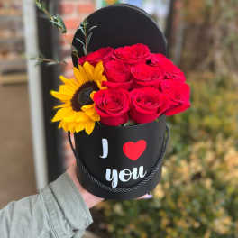 Red roses and a sunflower in a black heart-shaped box