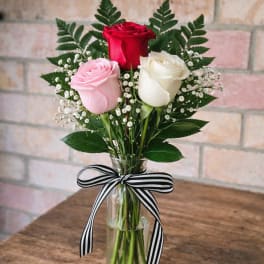 Three roses in a glass vase with a striped ribbon