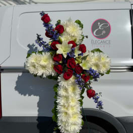 Cross-shaped floral tribute with red roses, white chrysanthemums, and blue flowers