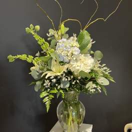 Tall white and pale blue floral arrangement in a glass vase
