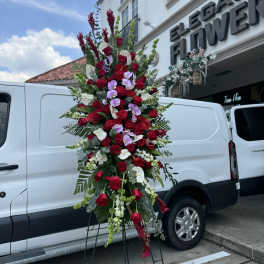 Tall standing floral spray with red roses and purple orchids on an easel