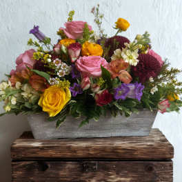 Mixed bouquet in a gray rectangular container with pink, yellow, purple, and white blooms