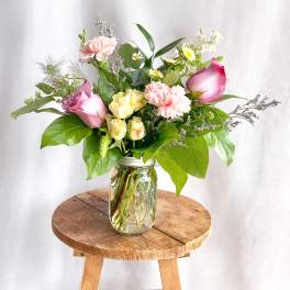 Pink and yellow roses with carnations in a glass jar vase