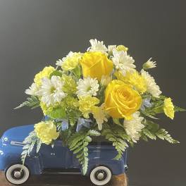 Yellow roses and white daisies arranged in a blue toy truck