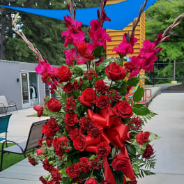 Tall red floral standing arrangement with roses and gladiolus on a metal easel
