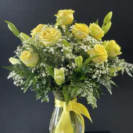 Yellow roses and lilies in a clear glass vase with a yellow ribbon