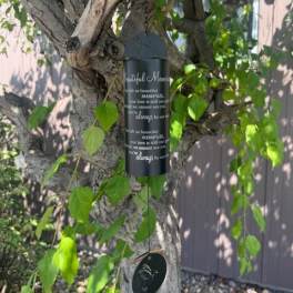 Black memorial wind chime hanging from a tree branch