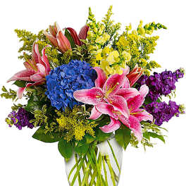 Bouquet of pink lilies, blue hydrangea, and purple flowers in a glass vase
