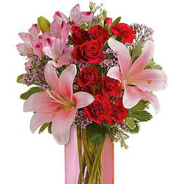 Pink lilies and red roses in a tall glass vase with a pink ribbon