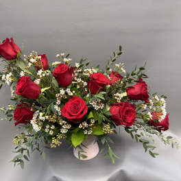 Red roses arranged in a low white vase with small white filler flowers