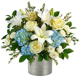 White lilies and cream roses with blue hydrangeas in a silver vase