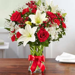 Red roses and white lilies arranged in a glass vase with a red ribbon