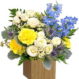 Bouquet of white roses, yellow blooms, and blue flowers in a wooden box
