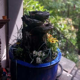 Blue planter with a small rock fountain and mixed flowers