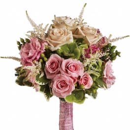 Hand-tied bouquet of cream and pink roses with green hydrangeas and a pink ribbon-wrapped stem.