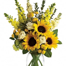 Tall arrangement of yellow sunflowers, white roses, and yellow flowers in a clear glass vase