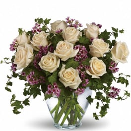 Arrangement of cream roses with small purple flowers in a clear glass vase