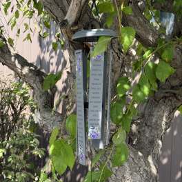 Hanging memorial wind chime with purple floral accents on a tree