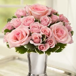 Arrangement of light pink roses in a tall silver vase on a tray.