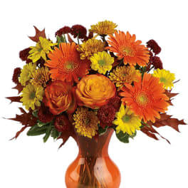 Arrangement of orange gerbera daisies, roses, and yellow mums in an orange glass vase
