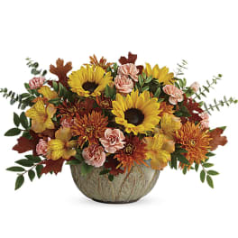 Low centerpiece of sunflowers, orange mums, and pink carnations in a green ceramic bowl