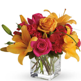 Low arrangement of yellow lilies and hot pink roses in a clear glass cube vase