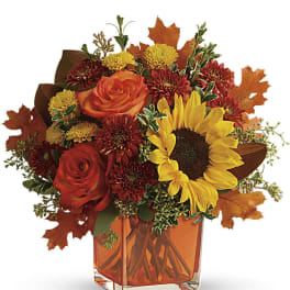 Autumn bouquet with sunflower, orange roses, and mums in an orange glass cube vase