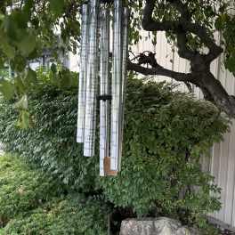 Silver memorial wind chimes hanging from a tree in a garden