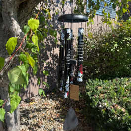 Black memorial wind chime hanging outdoors among trees and shrubs