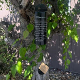 Black memorial wind chime hanging from a tree branch