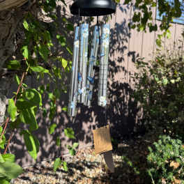 Decorative silver wind chime with blue butterflies and white flowers hanging from a tree branch