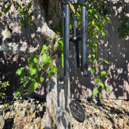 Black metal wind chime with memorial message hanging from a tree outdoors.